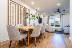 A dining area with a wooden table and chairs, a flat-screen TV, and a view of the outdoors.