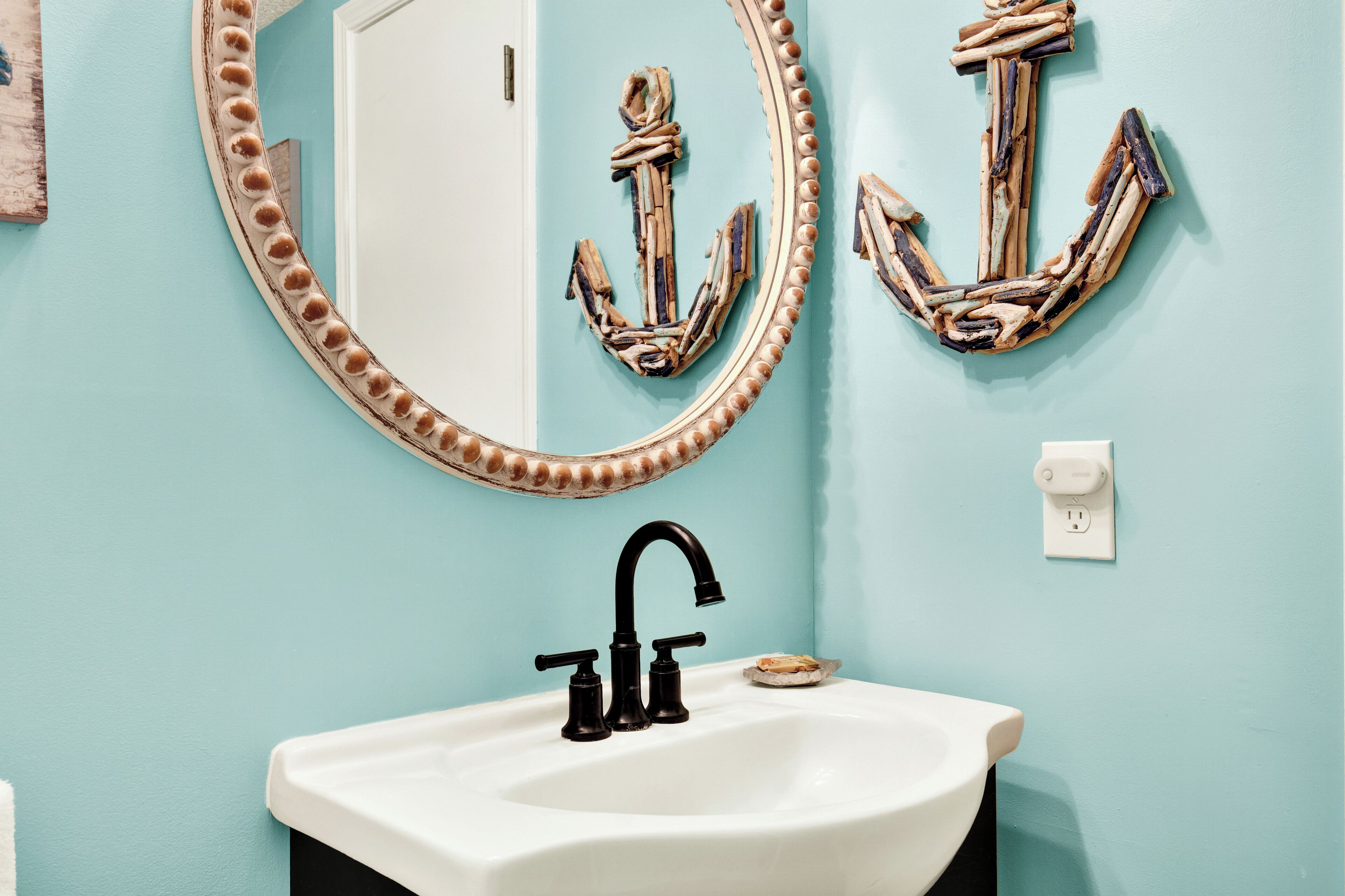 A bathroom with a white sink, black faucet, and two decorative anchors on the wall.