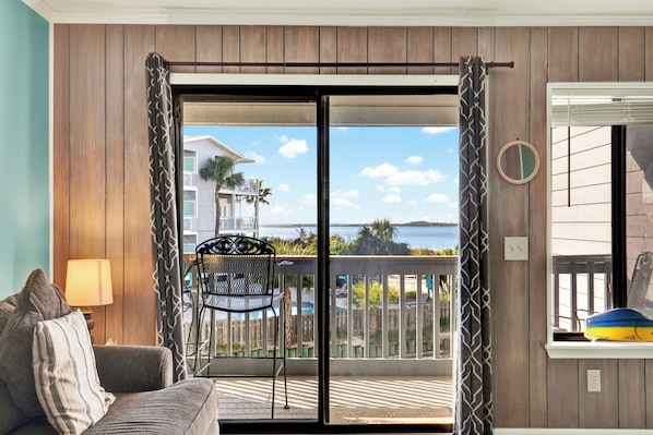 A balcony with a view of the sea, a chair, and a table with a lamp.