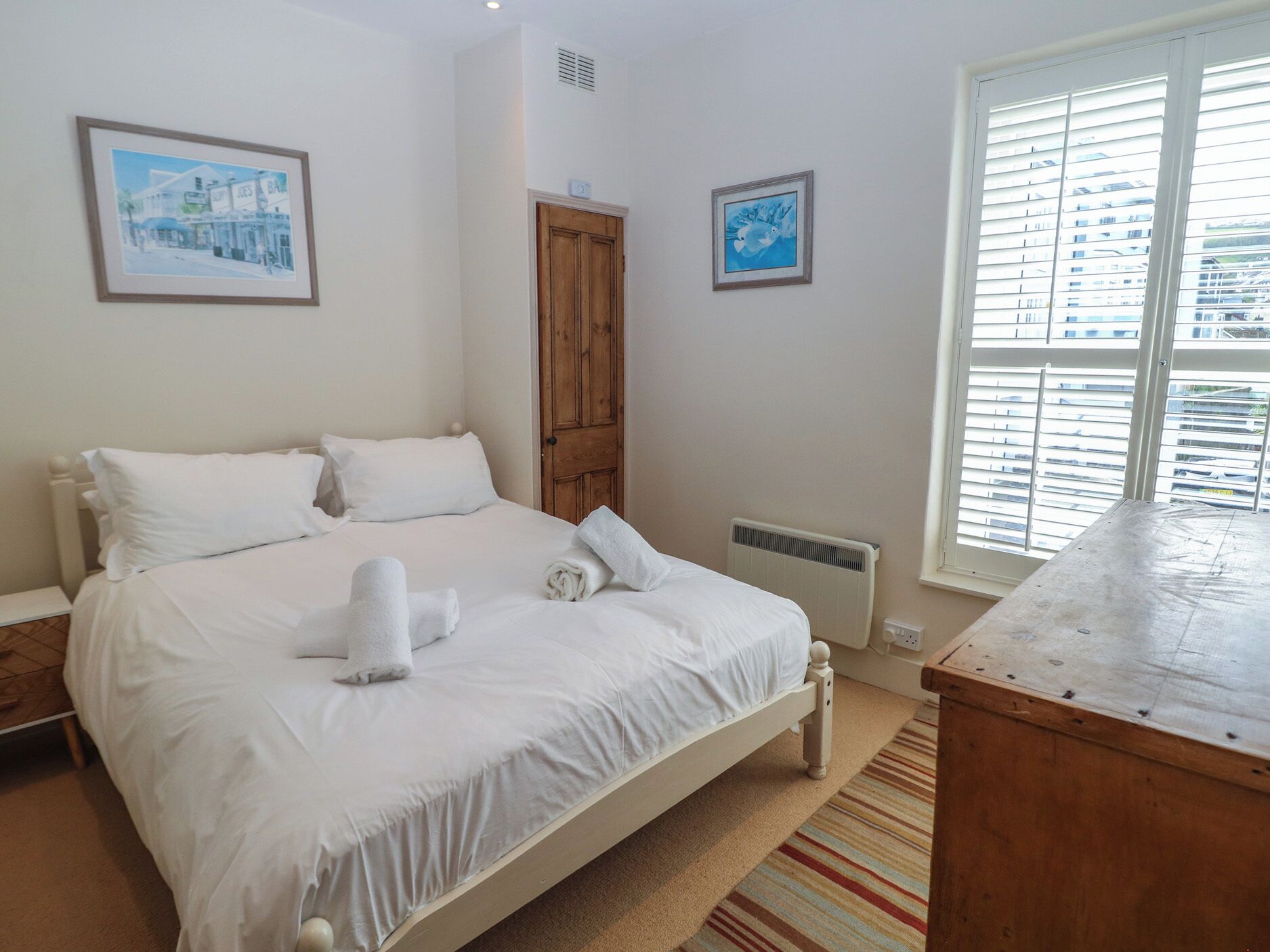 A bedroom with a bed, a wooden door, a radiator, and a window with blinds.