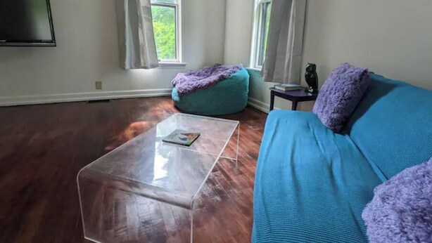 Ein Wohnzimmer mit einem blauen Sofa, einem türkisfarbenen Sitzsack, einem Glastisch und einem flachbildfernseher, der an der Wand befestigt ist.