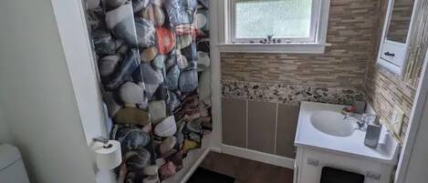 A bathroom with a stone-patterned shower curtain, a window, a sink, and a mirror.