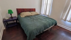 Ein Schlafzimmer mit einem Bett, einem Nachttisch, einer Lampe und einem Fenster mit Vorhängen.
