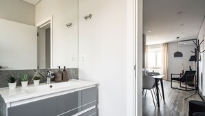 Een moderne badkamer met een grote spiegel, een wit aanrecht en grijze kastjes. Er staan potplanten op het aanrecht.