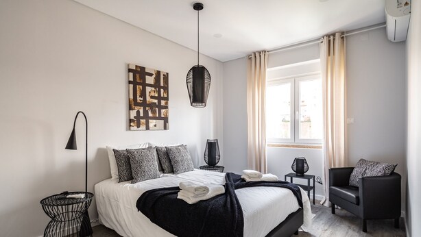 Een moderne slaapkamer met een bed, nachtkastjes, een stoel en een raam met gordijnen.
