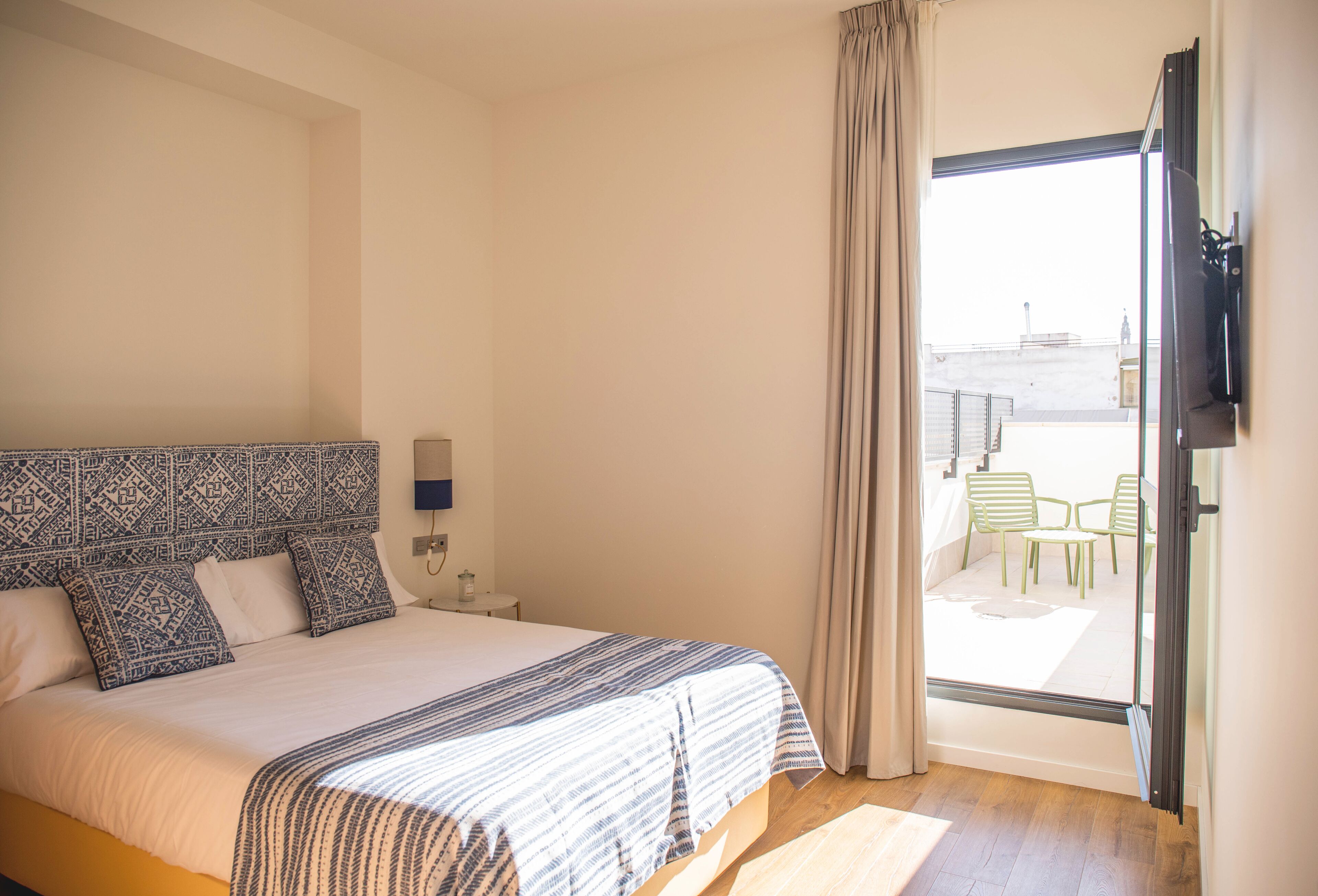 Een hotelkamer met een groot bed, een aan de muur bevestigde televisie en een balkon met stoelen en een tafel.