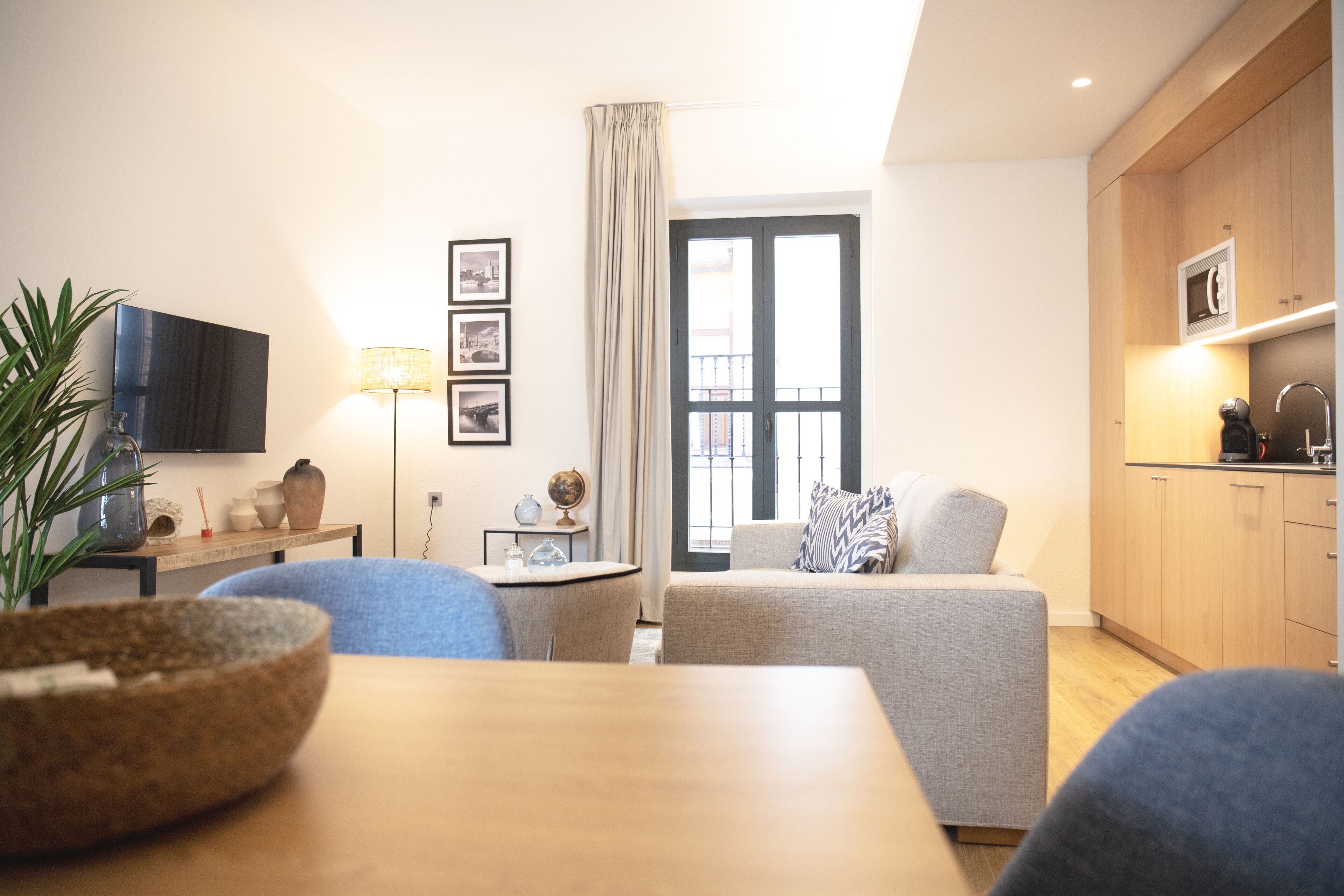 A modern living room with a sofa, a dining table, and a kitchen area with wooden cabinets.