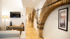 A modern interior with a wooden floor, a flat-screen TV mounted on the wall, a sofa, a lamp, and a framed picture. - nQn Aparts & Suites Sevilla (Seville)