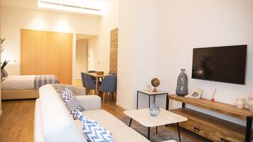 Un salon moderne comprenant un canapé, une table à manger avec des chaises, un téléviseur fixé au mur et une armoire en bois.