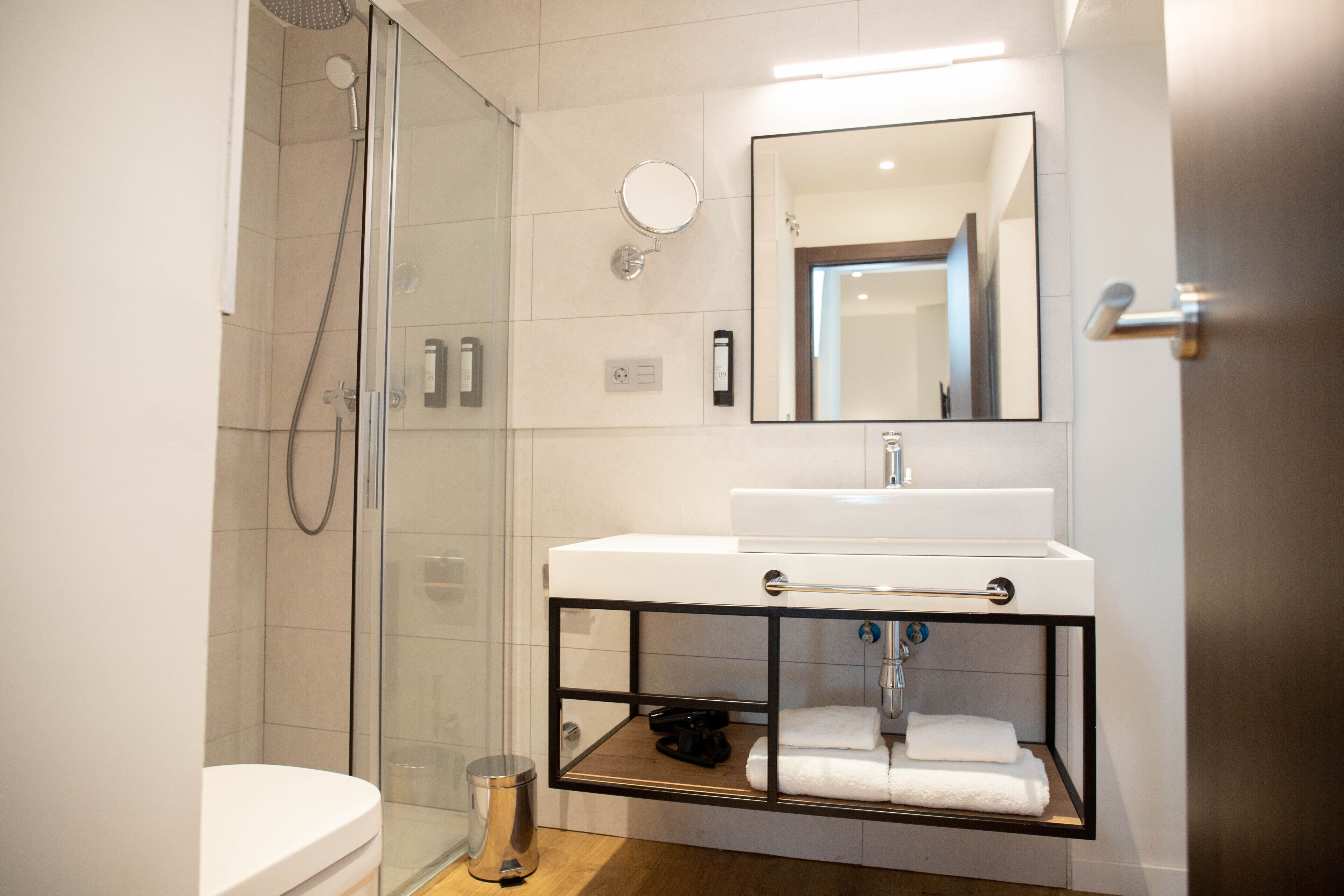 A modern bathroom with a glass shower enclosure, a white sink with a mirror above it, and a small shelf under the sink.