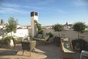 A rooftop patio with wicker furniture, potted plants, and a view of the cityscape. - nQn Aparts & Suites Sevilla (Seville)