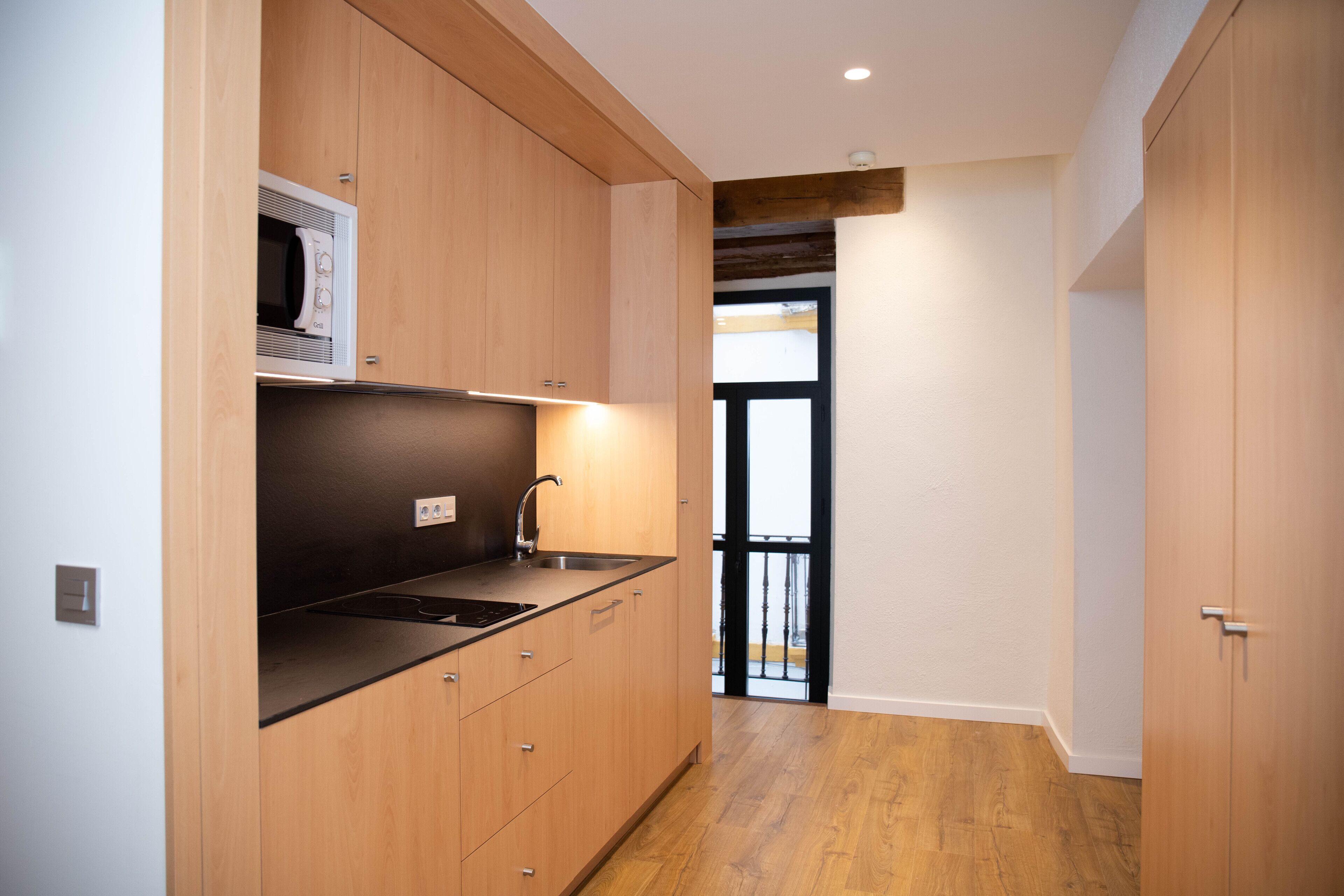 A compact kitchen with wooden cabinets, a black countertop, and a built-in microwave.