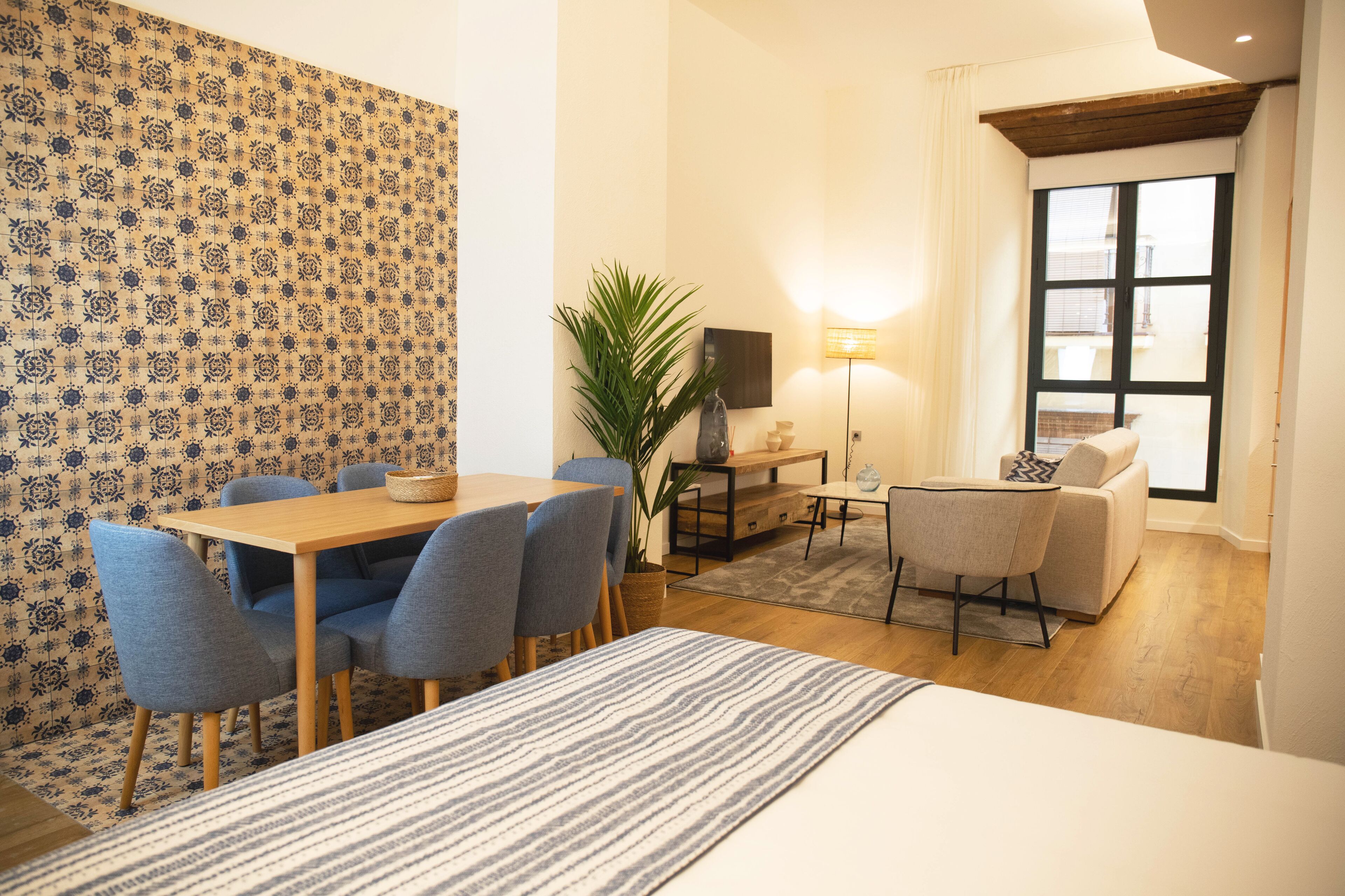 Habitación de hotel con comedor, sofá, televisión y un gran ventanal.
