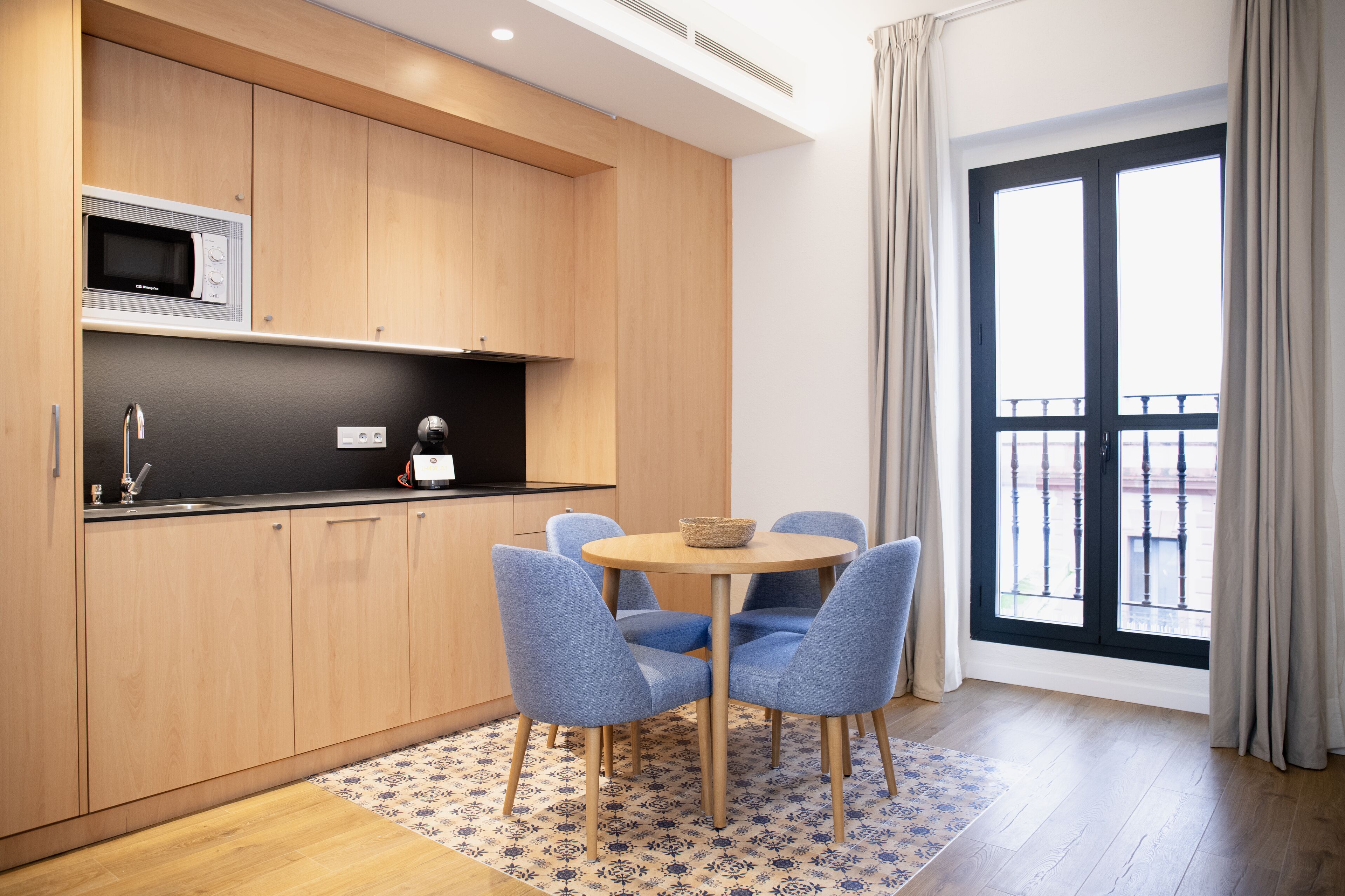 A modern kitchen with wooden cabinets, a microwave, and a dining area with blue chairs and a round table.
