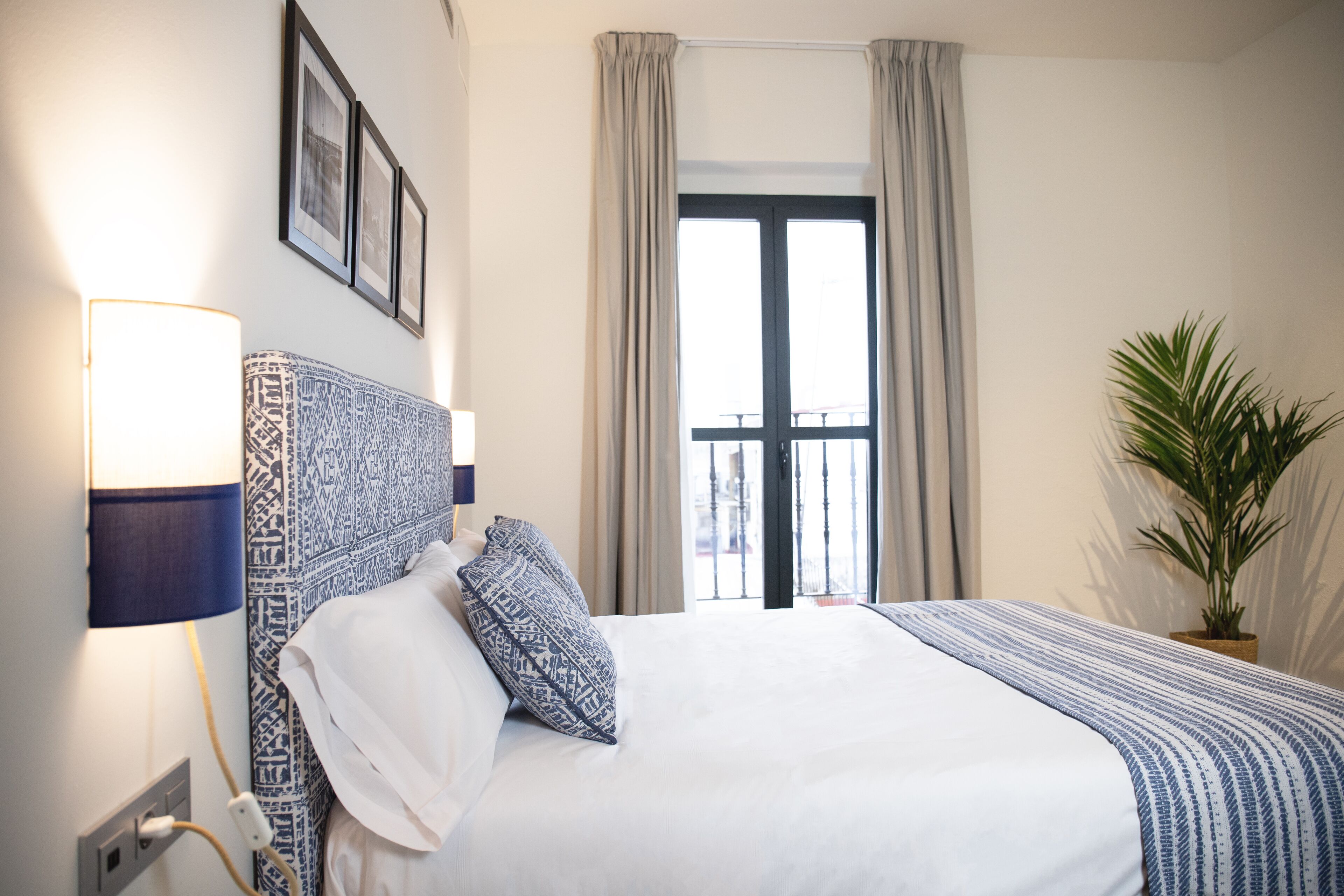 A neatly made bed with patterned pillows, a bedside lamp, and a potted plant.