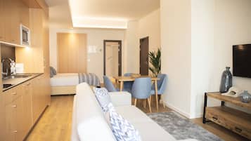 Una sala de estar moderna con un sofá, un comedor con sillas, una cocina con armarios de madera y un televisor montado en la pared.