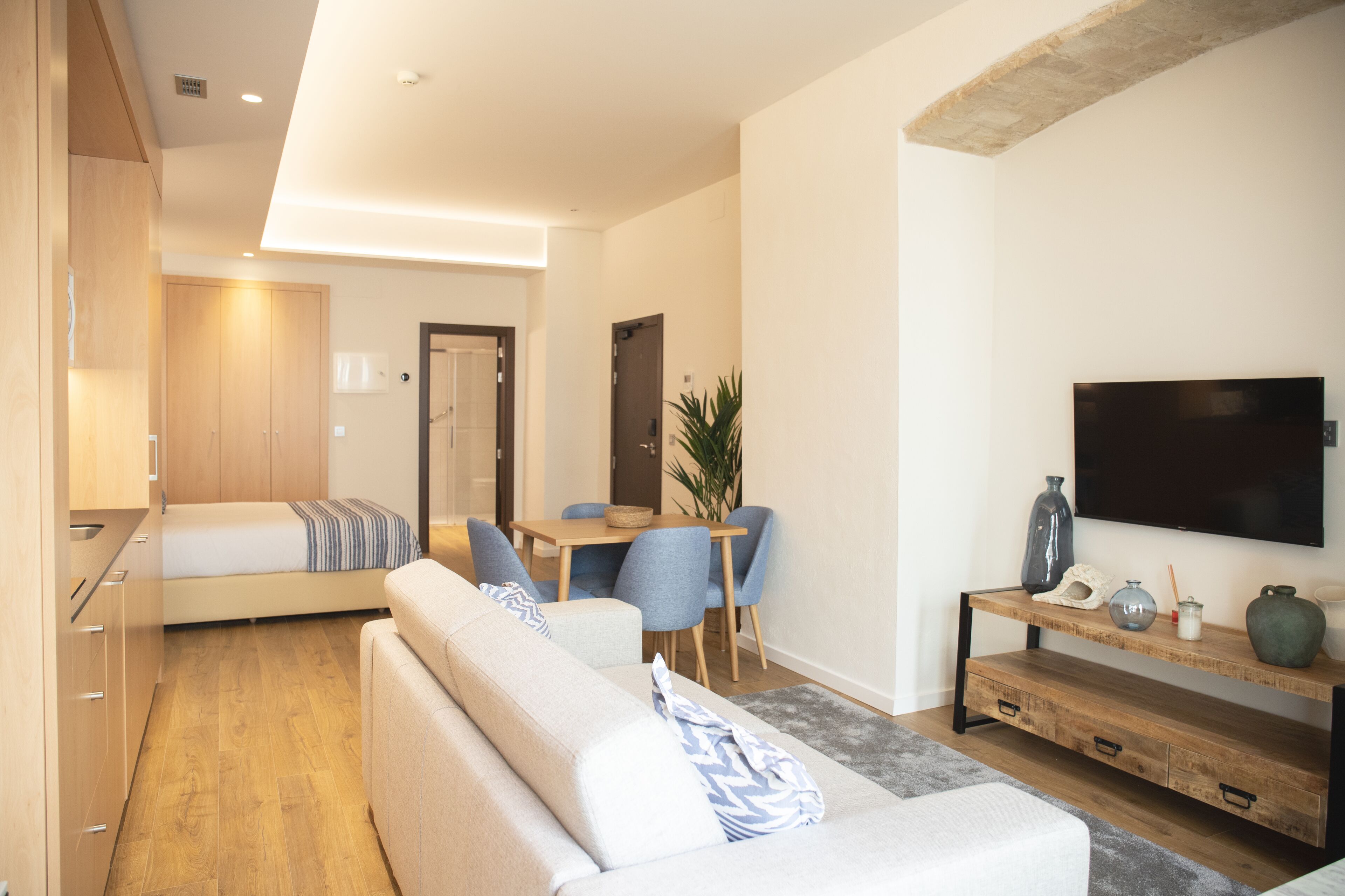 Una habitación de hotel moderna con sofá, mesa de comedor, sillas, televisor y una pequeña cocina.