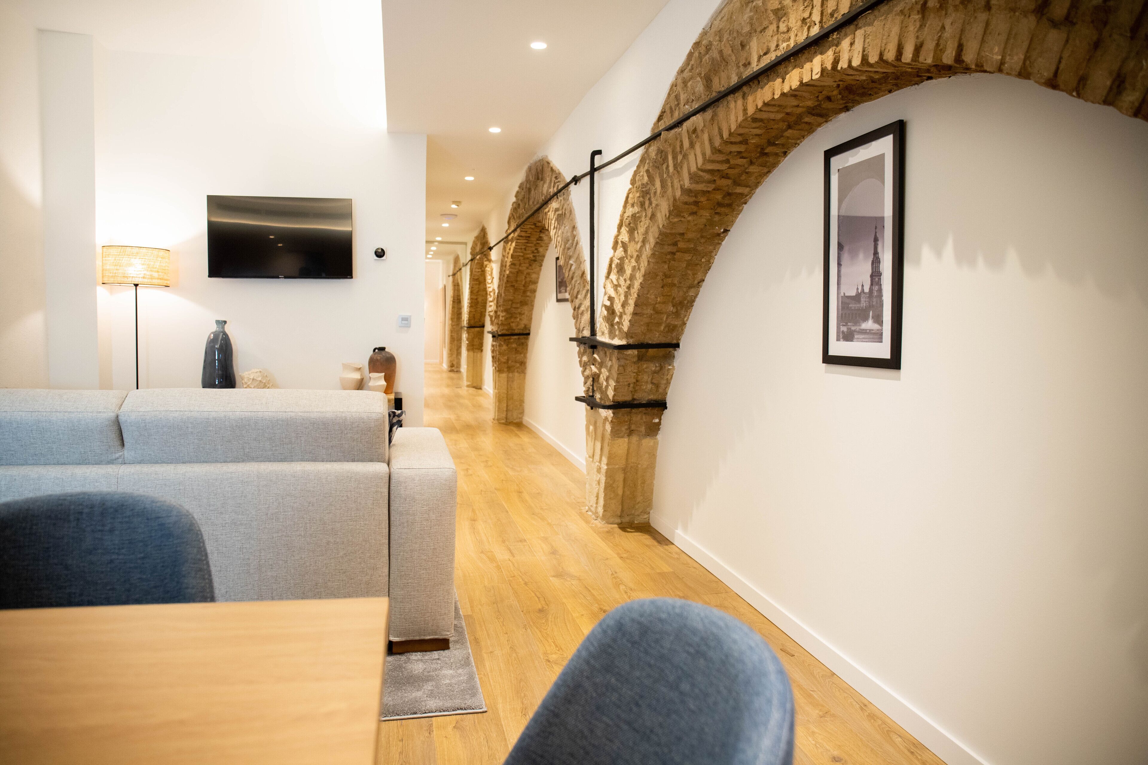 A modern interior with a long hallway, wooden flooring, and a seating area with sofas and a table.