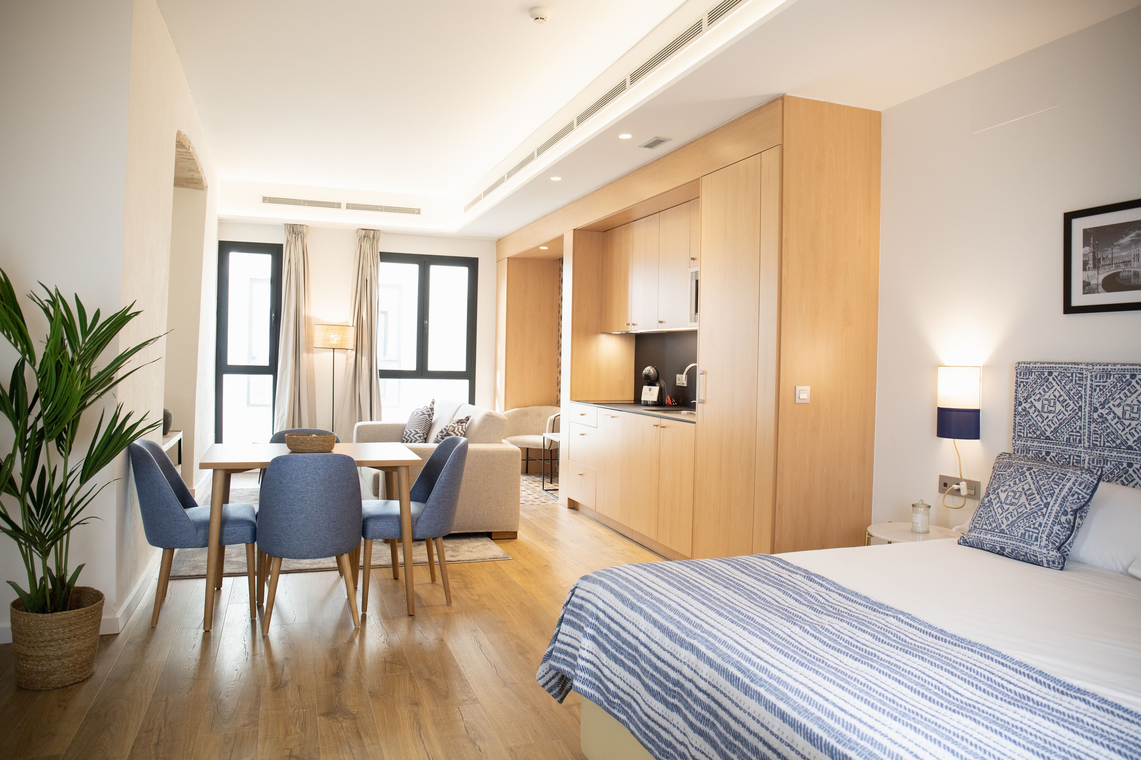 Een moderne hotelkamer met een bed, een zithoek met stoelen en een tafel, een kitchenette en een groot raam.