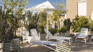A rooftop terrace with white lounge chairs, a large umbrella, and potted plants. - nQn Aparts & Suites Sevilla (Seville)