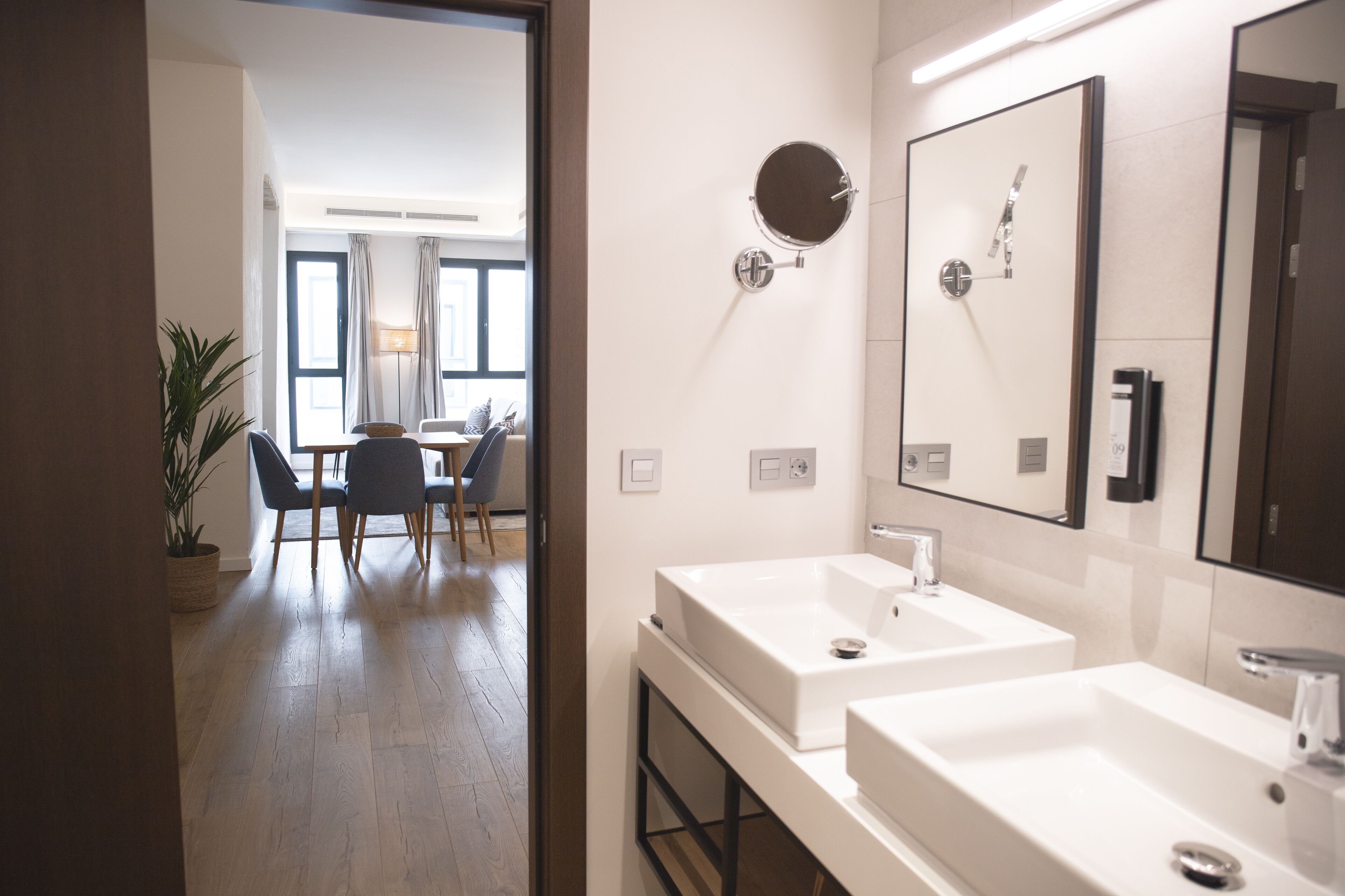 A modern bathroom with two sinks, a large mirror, and a potted plant.