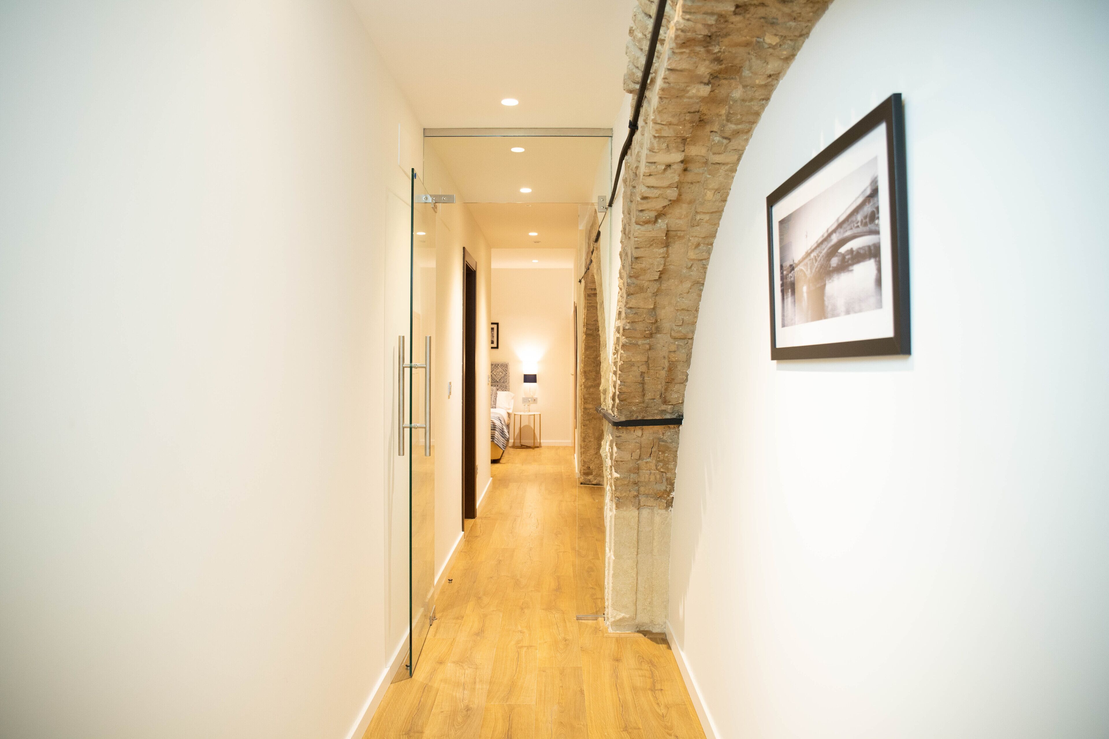 A hallway with a wooden floor, white walls, and a stone accent wall.