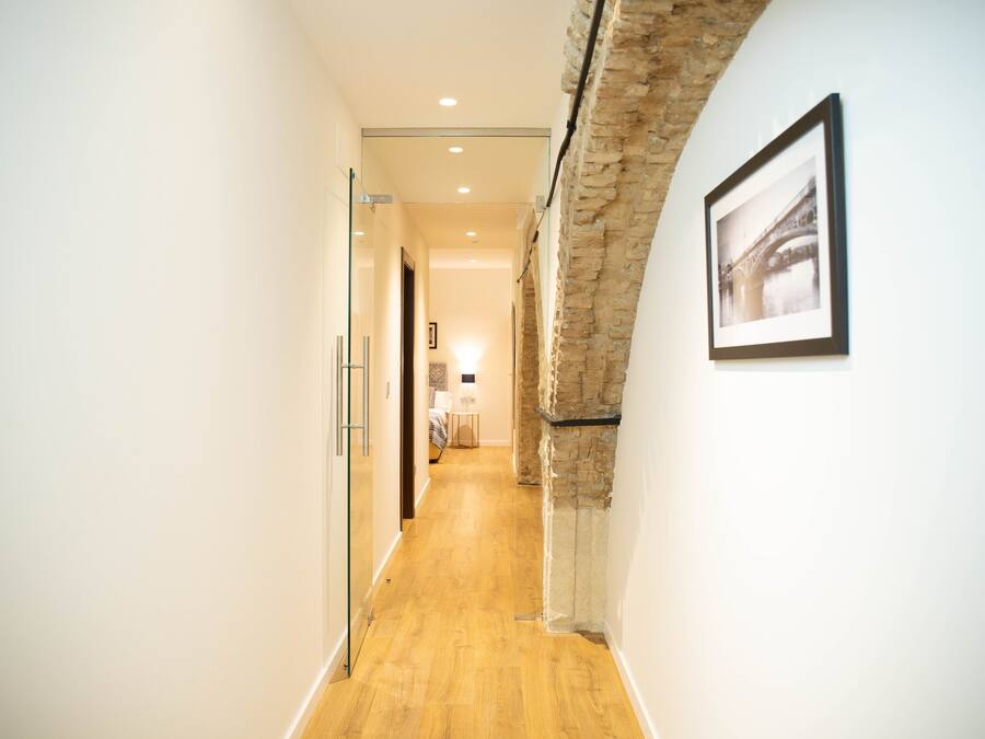 A hallway with a wooden floor, white walls, and a stone accent wall.