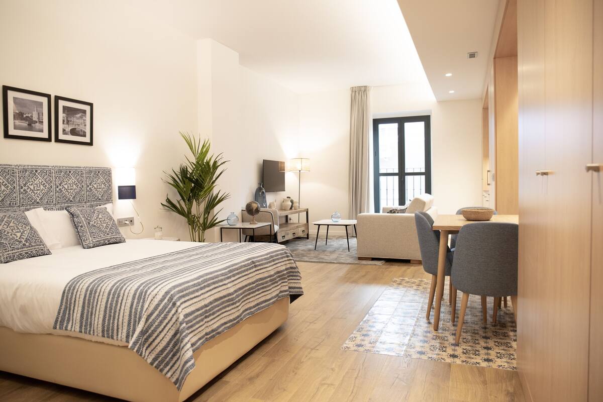 A modern hotel room with a large bed, a desk, a chair, and a dining table.