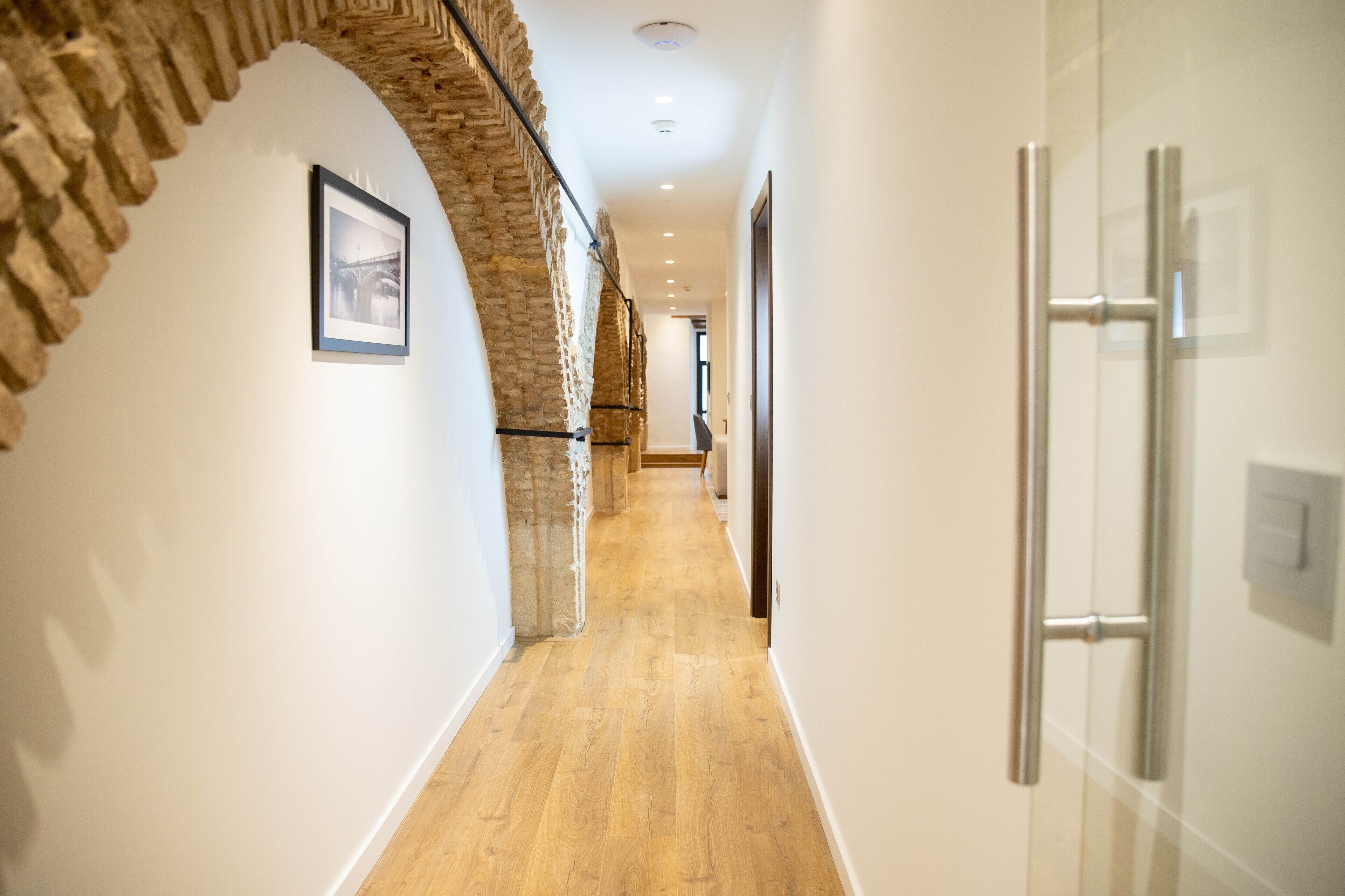 A hallway with a wooden floor, white walls, and a stone archway.