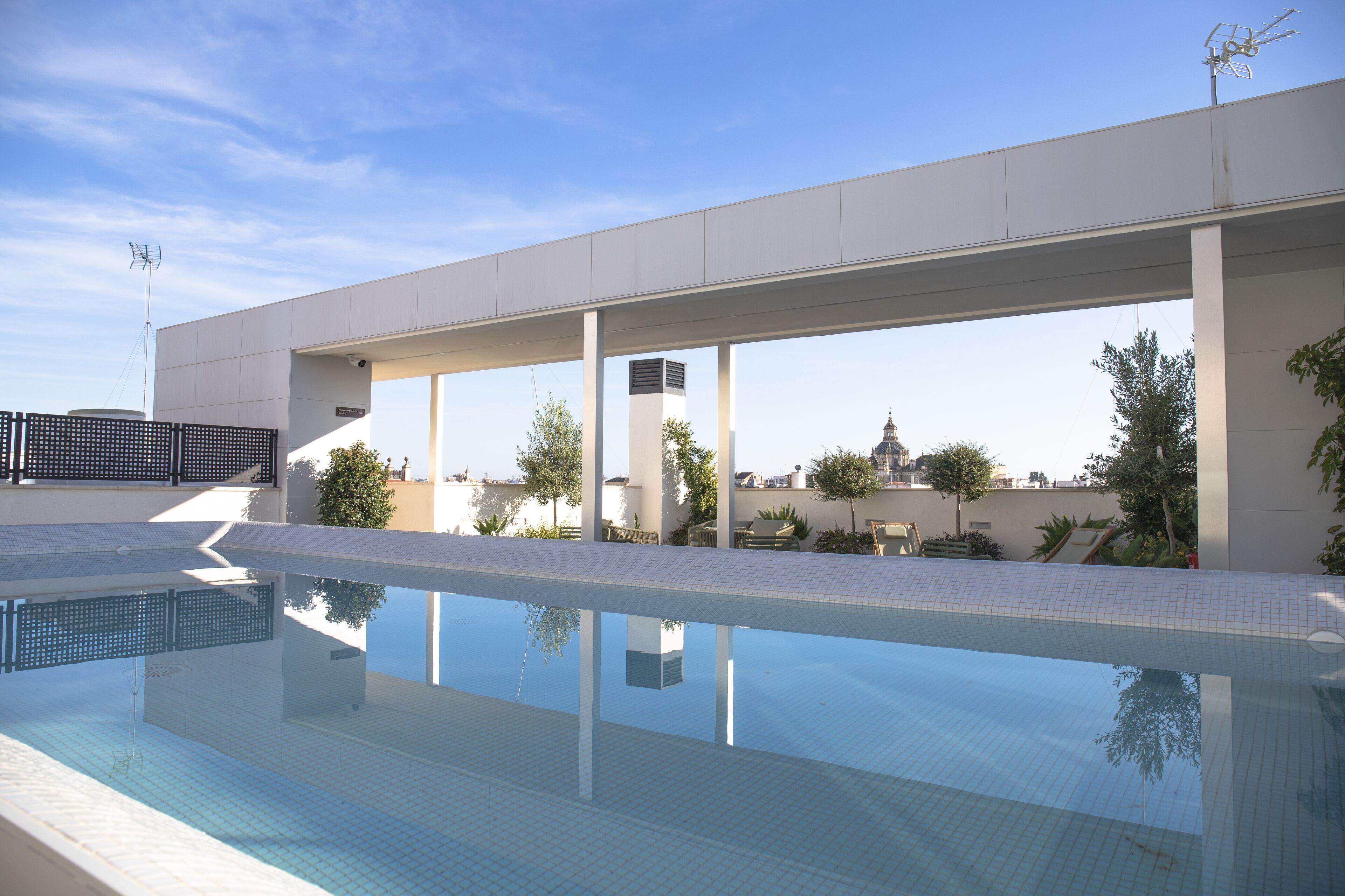 Ein moderner, überdachter Swimmingpool mit klarem, blauem Wasser, umgeben von einem weißen Fliesenbelag und einer niedrigen weißen Mauer.