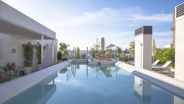A modern swimming pool with clear water, surrounded by lounge chairs and potted plants. - nQn Aparts & Suites Sevilla (Seville)