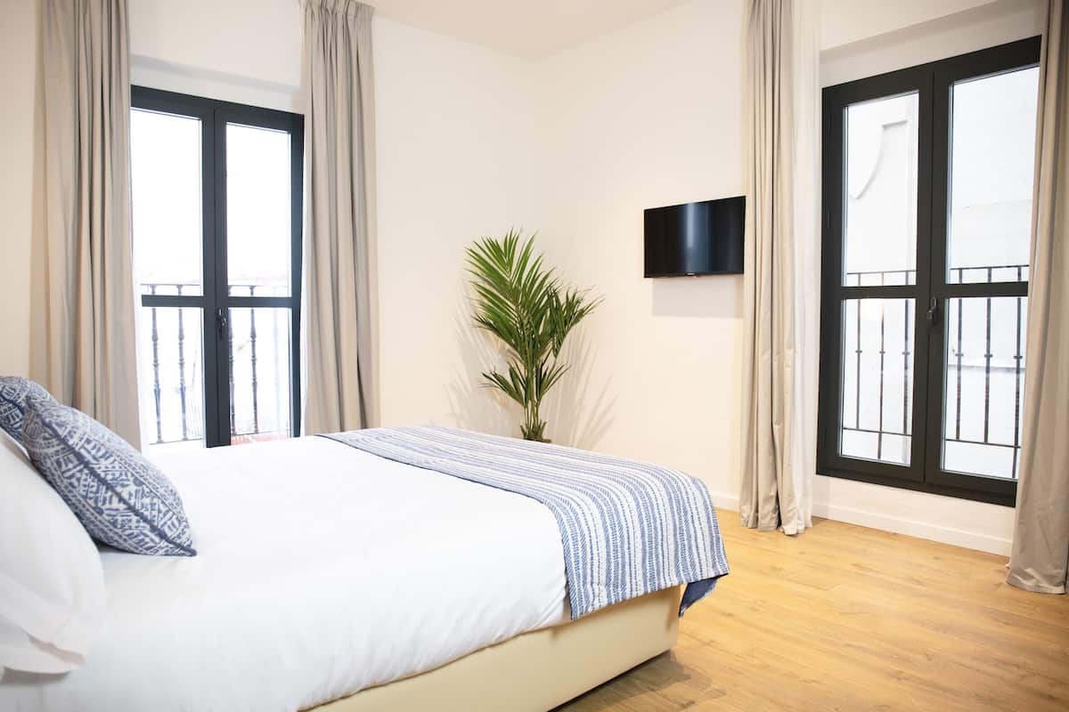 A bedroom with a bed, curtains, a potted plant, and a TV on the wall.