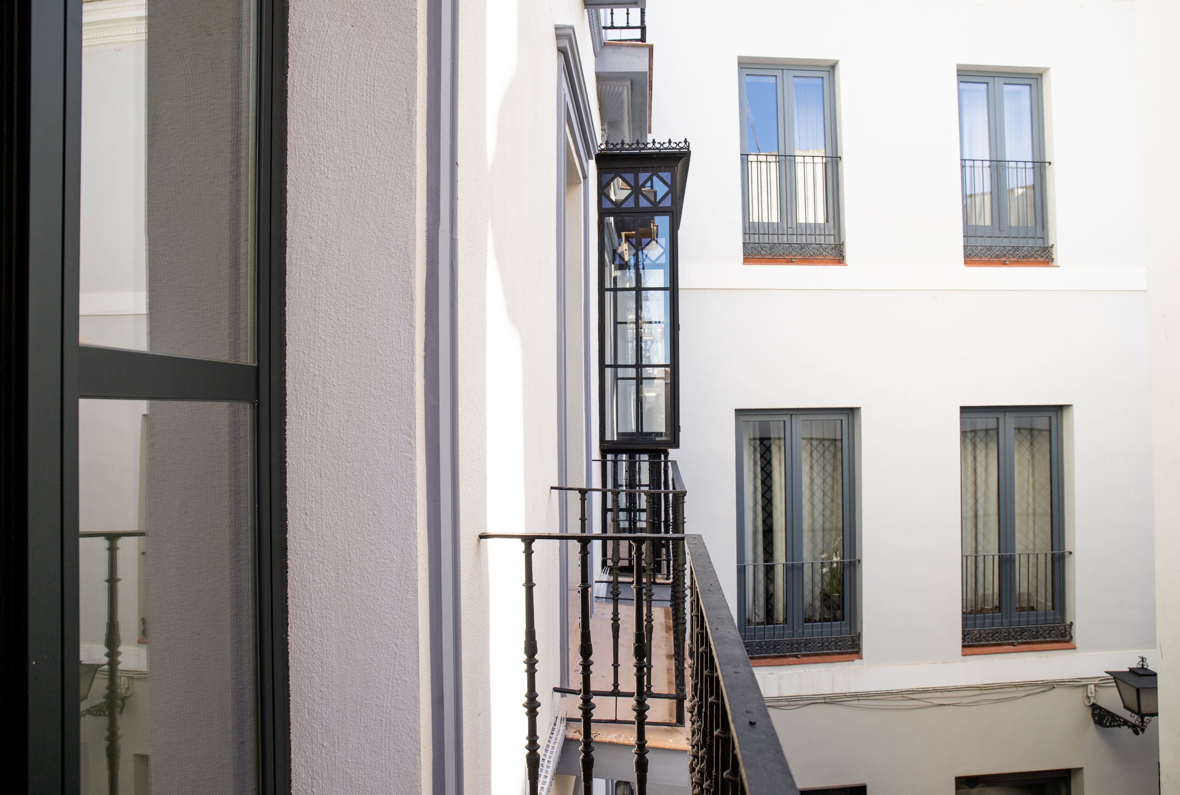 Un edificio con fachada blanca, barandillas negras y varias ventanas con cortinas.
