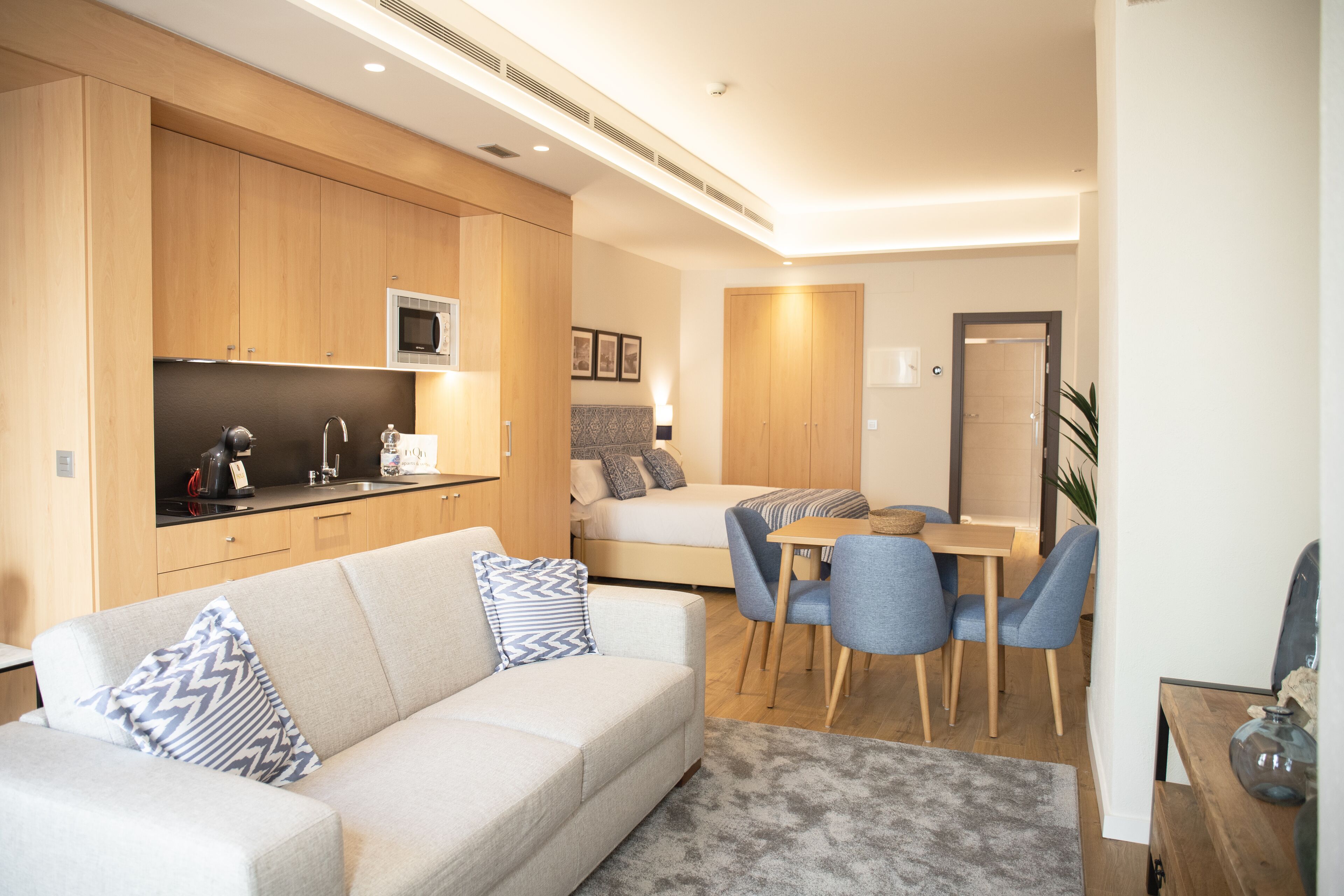 A compact living space with a kitchenette, a sofa with patterned cushions, a dining area with chairs, and a bed.