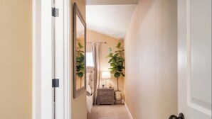 A narrow hallway with a bed, bedside table, lamp, and two potted plants. - Patio w/ fire pit home ✶ 10min to DT → Has it all! (Portland)