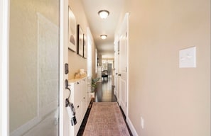 A narrow hallway with a patterned rug, a coat rack, and a door at the end. - Patio w/ fire pit home ✶ 10min to DT → Has it all! (Portland)