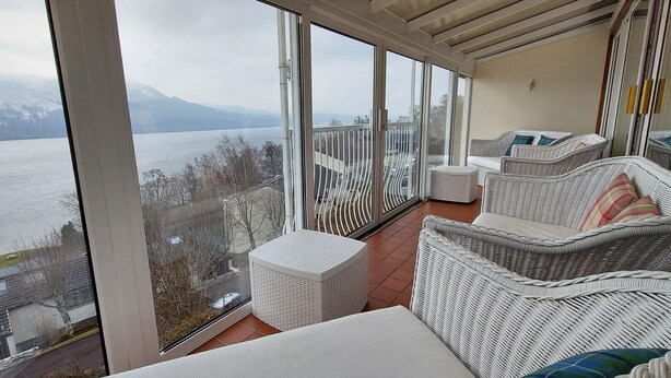 A balcony with wicker furniture, a white table, and a view of a lake and mountains. - Loch Rannoch Highland Club Highland Lodge 33 (Kinloch Rannoch)
