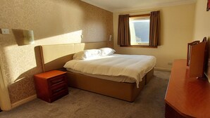 A hotel room with a bed, a nightstand, a dresser, and a window with curtains. - Loch Rannoch Highland Club Highland Lodge 33 (Kinloch Rannoch)