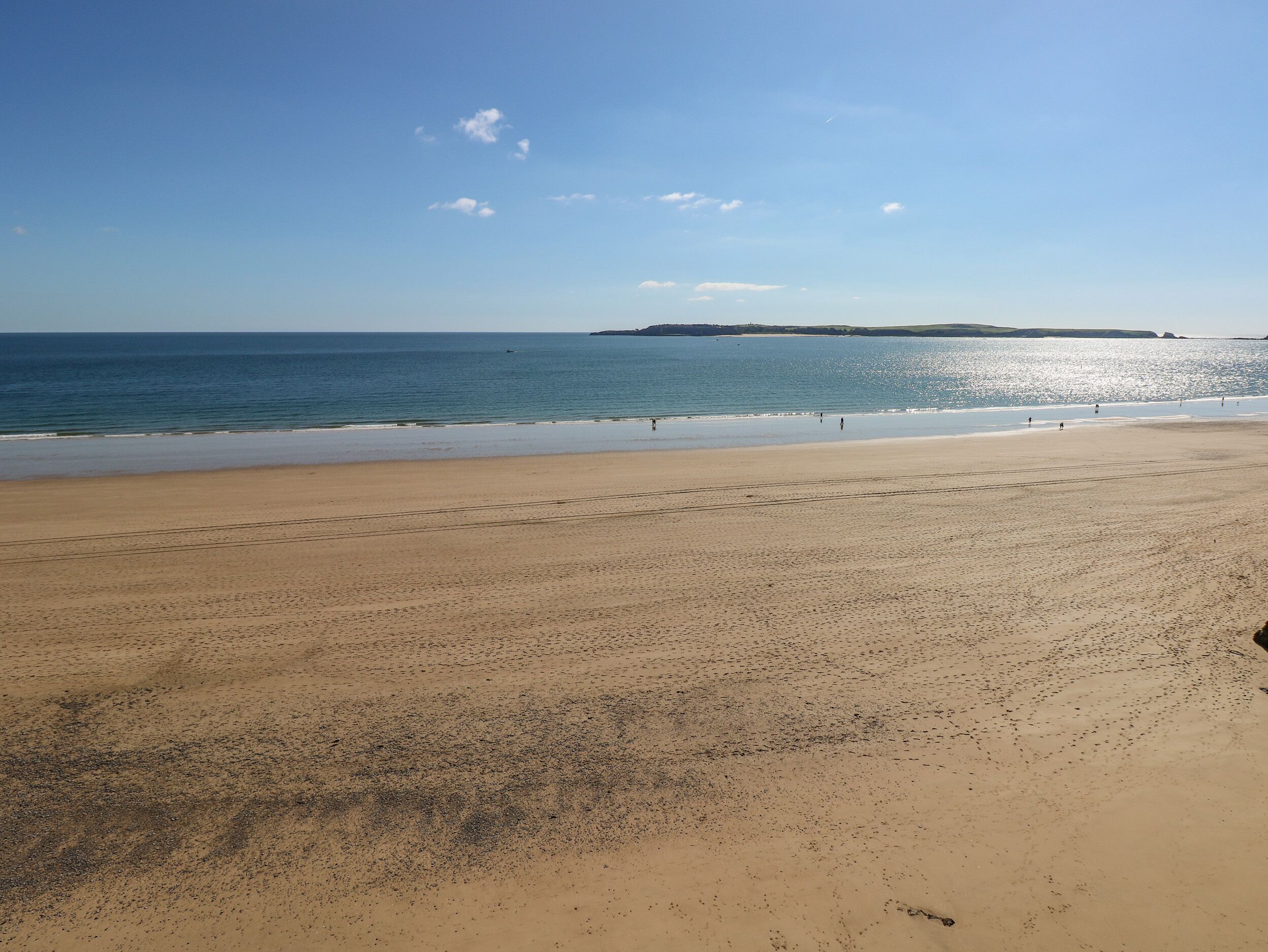 Ein weiter Sandstrand mit blauem Himmel und ruhiger See.