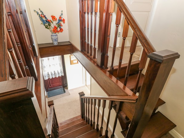 A wooden staircase with a handrail, leading to a landing with a vase of flowers and a door.