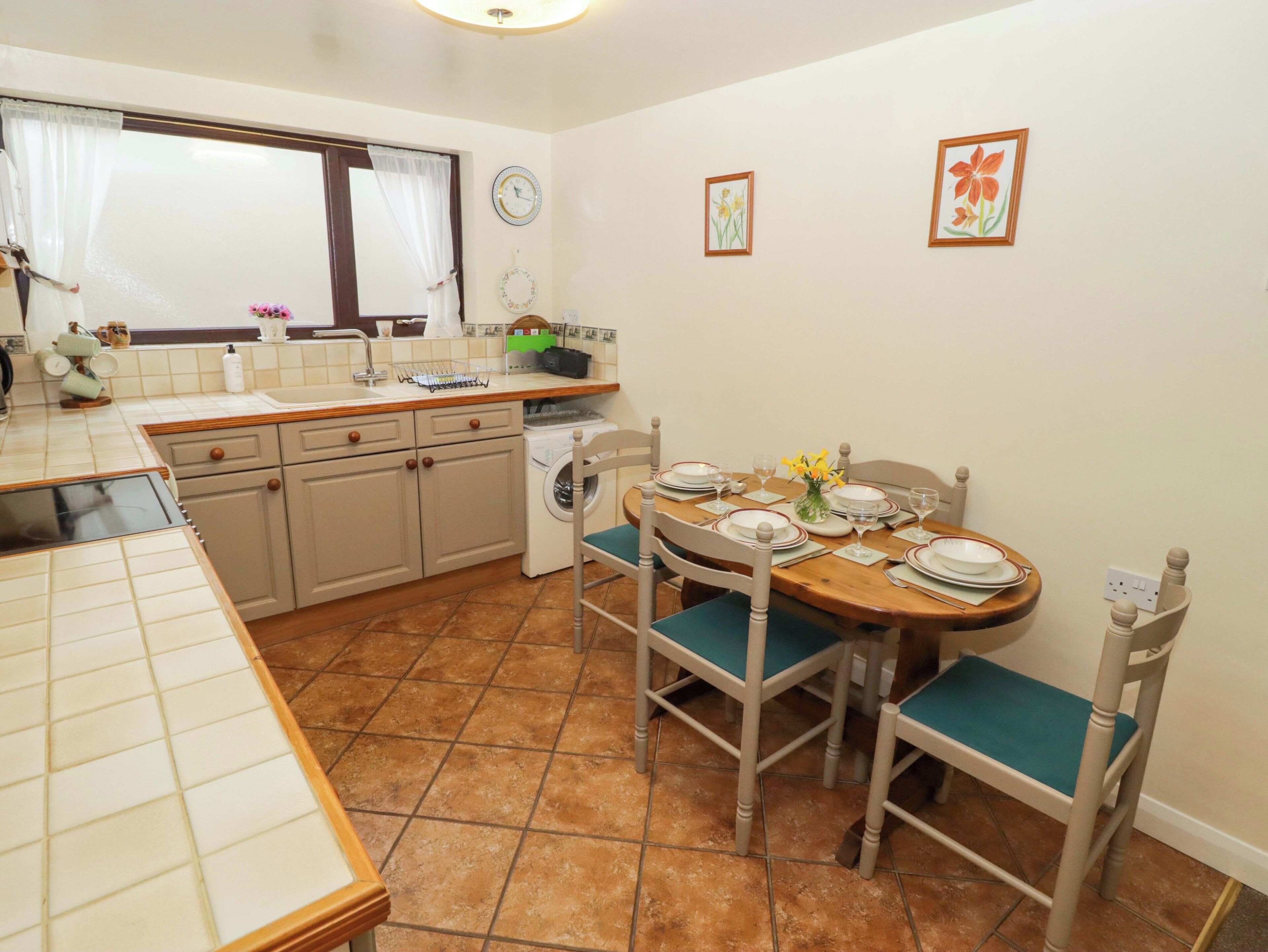 A compact kitchen with a dining area, featuring a sink, cabinets, a washing machine, and a dining table set for four.
