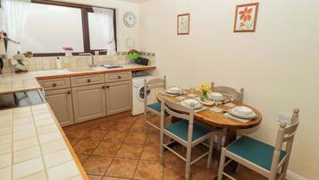 A compact kitchen with a dining area, featuring a sink, cabinets, a washing machine, and a dining table set for four.