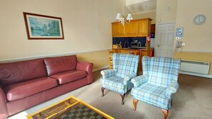 A living room with a red sofa, two plaid armchairs, a small coffee table, and a painting on the wall. - Loch Rannoch Highland Club Studio 2 (Kinloch Rannoch)