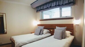 Une chambre d’hôtel avec deux lits simples, une fenêtre avec des rideaux et un miroir au mur.