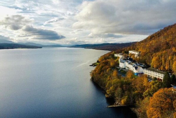 A lakeside property with a large building, surrounded by autumn foliage and a calm lake.