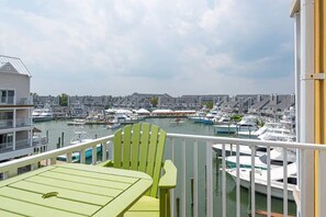 Un balcon donnant sur une marina remplie de bateaux, un bâtiment blanc et un ciel nuageux.