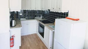 A compact kitchen with white cabinets, a microwave, a stove, and a refrigerator. - Loch Rannoch Highland Club Apartment 9 (Kinloch Rannoch)