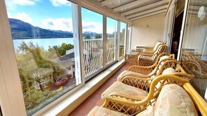 Un balcón con sillones de mimbre y vista a un lago y montañas.