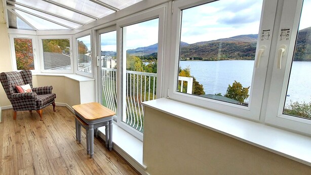 Ein Balkon mit Blick auf einen See und Hügel, ausgestattet mit einem Stuhl und einem kleinen Tisch.