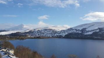 A lake surrounded by snow-covered mountains and a few buildings in the foreground.